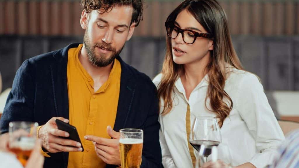 A man shows his phone to a woman while they sit at a table.
