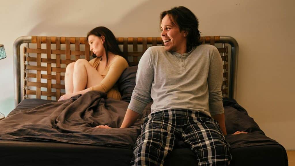 A happy man looks away from a sad woman sitting with her back to him.