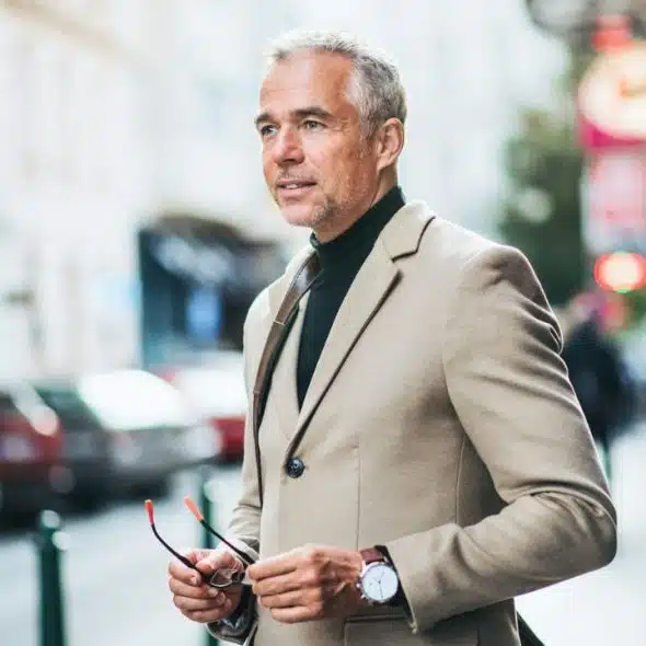 A middle-aged man in a beige suit stands on a city street.