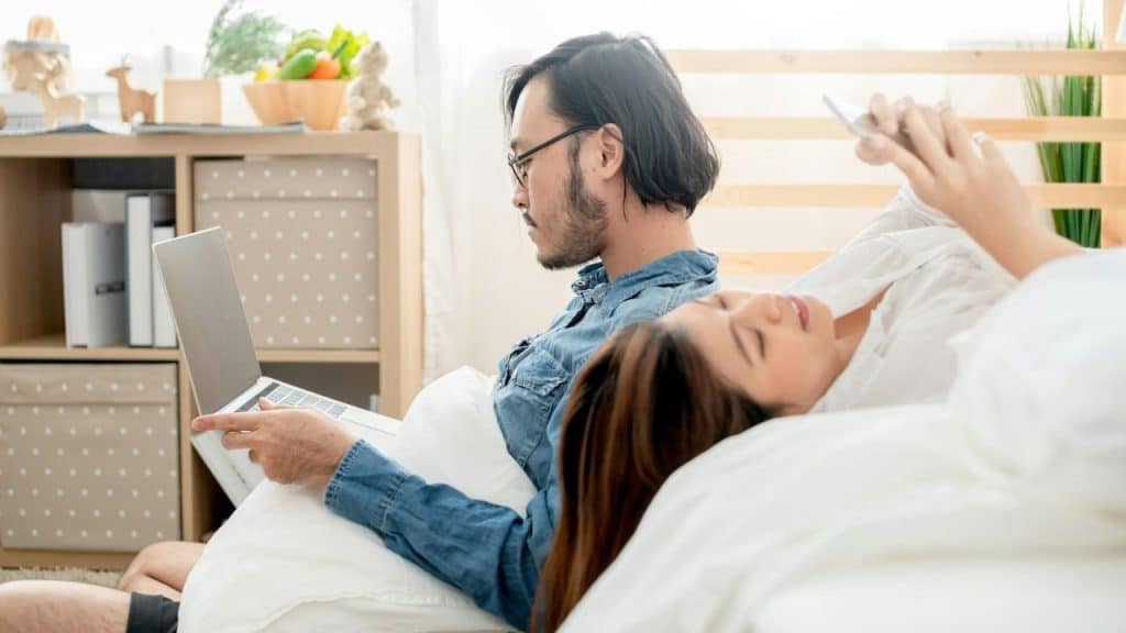 A busy man working on a laptop while a woman relaxes with her phone.