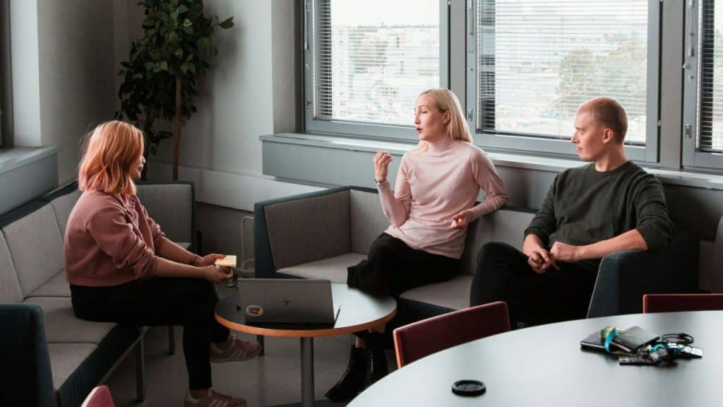 A blonde woman talks to a younger woman and a bald man in a modern office.