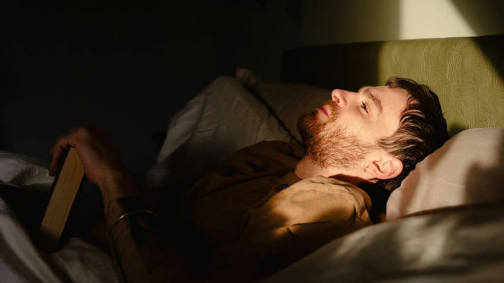 A contemplative man with a beard lying in bed, looking pensive.