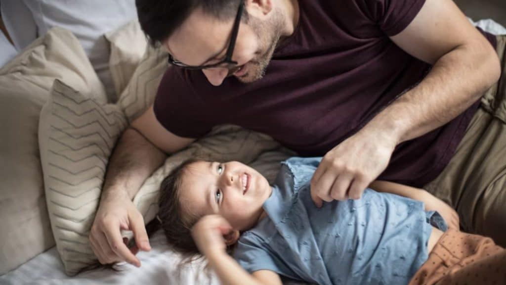 Man tucking a kid into bed with a smile