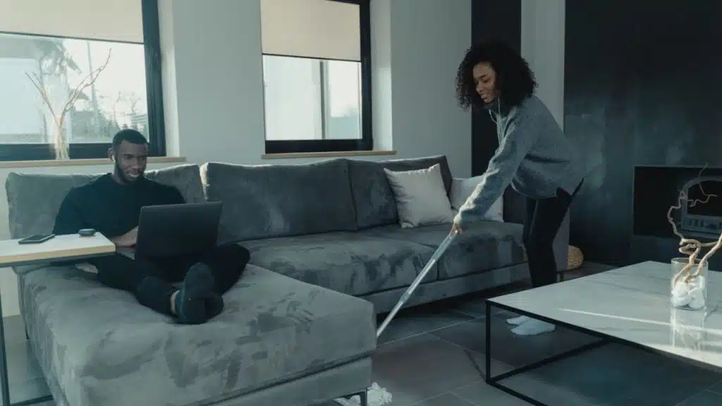 Woman organizing household tasks while man relaxes nearby.