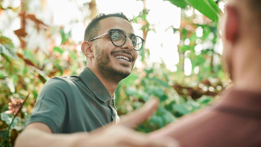 A man with glasses smiling amid lush greenery.