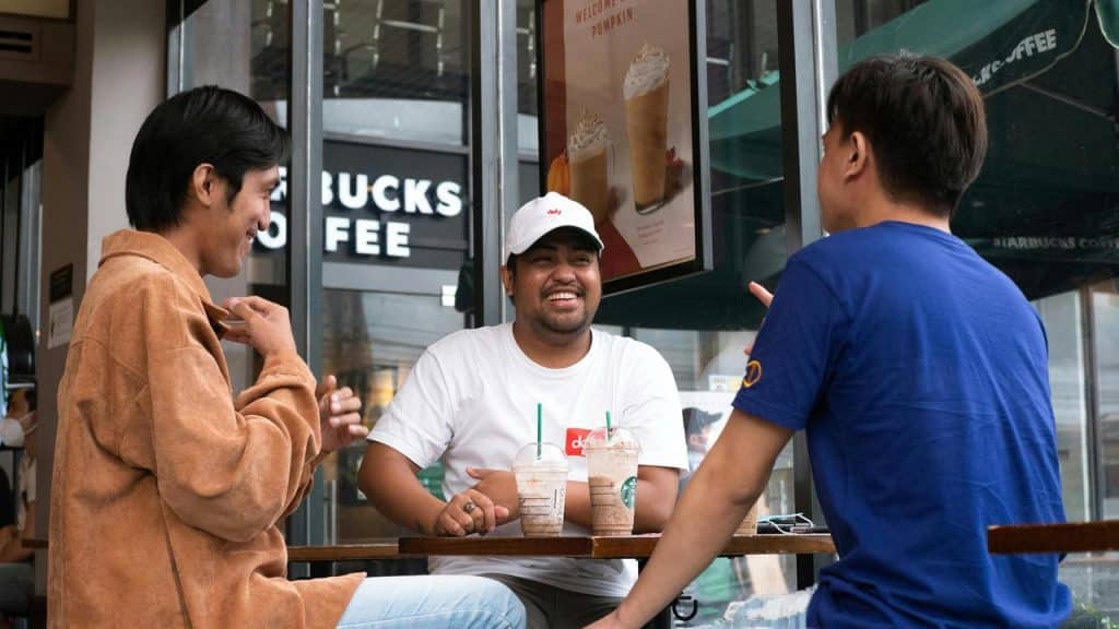 A trio of men chatting over iced coffees outside a coffee shop.