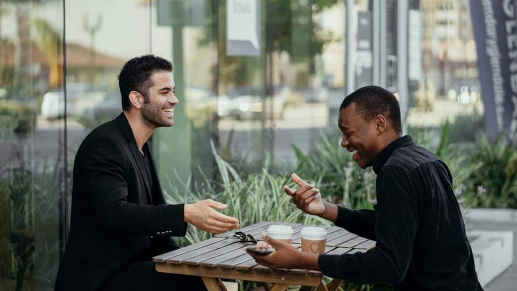 A pair of men sharing a laugh over coffee at an outdoor table.