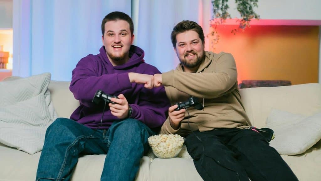 A pair of men fist bumping while playing video games on a couch.