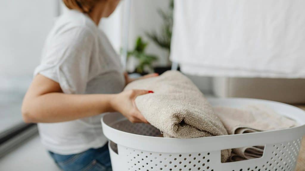 A person placing folded towels into a laundry basket.