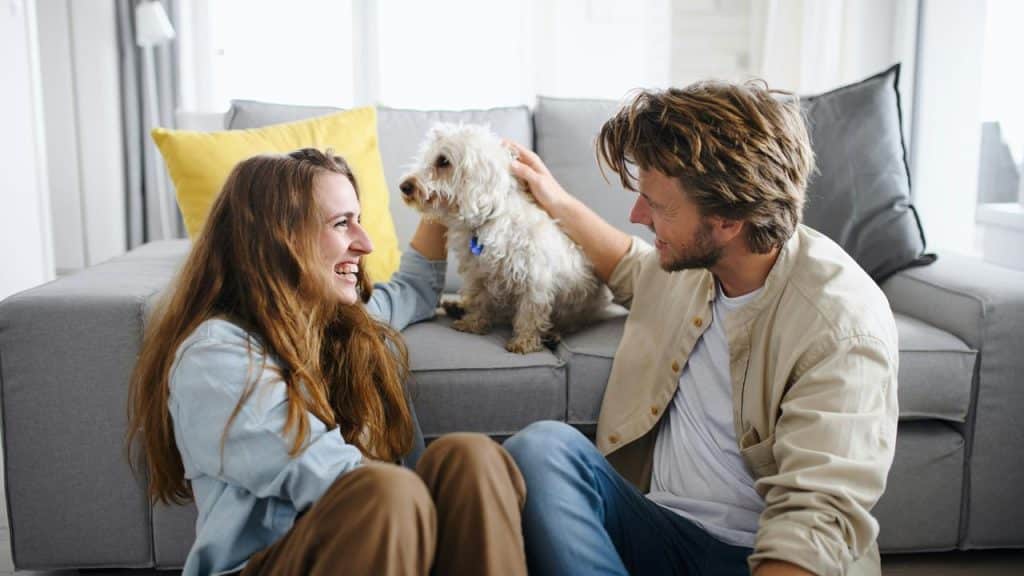A couple sitting on the floor petting their small dog.