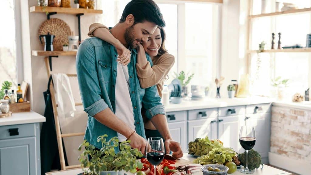 A couple cooking together in a sunlit kitchen.