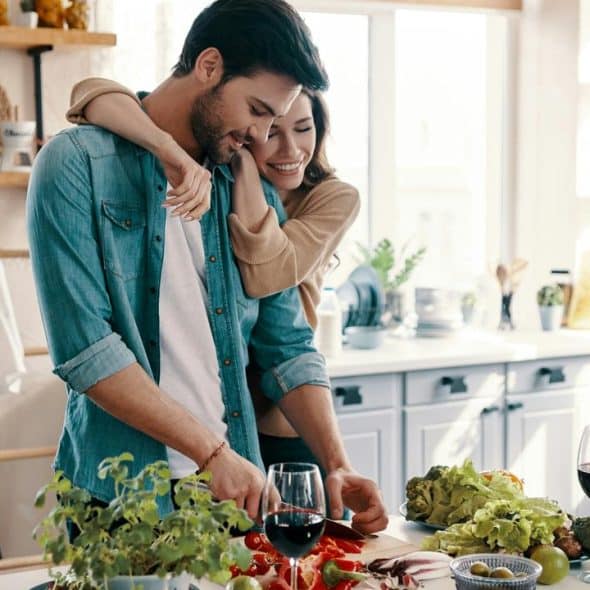 A couple cooking together in a sunlit kitchen.