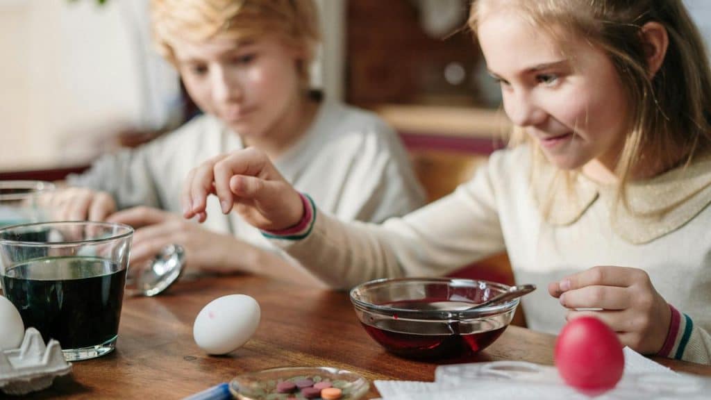 A girl dyeing an egg in a bowl of colored liquid.