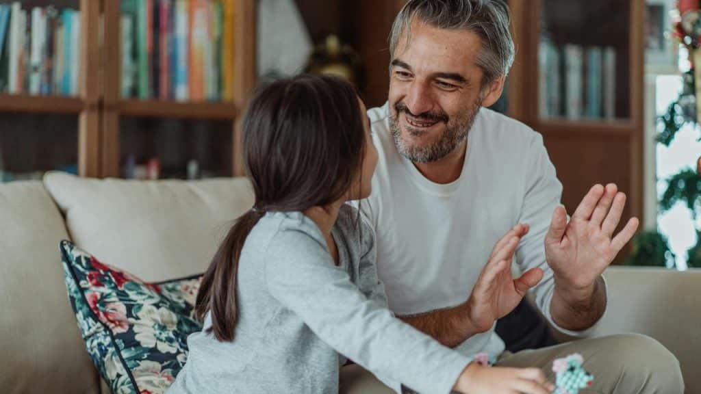 A father and daughter high-fiving on a couch.