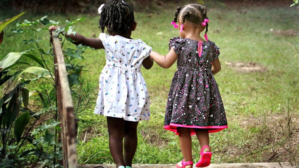 A pair of young girls holding hands as they walk outside.