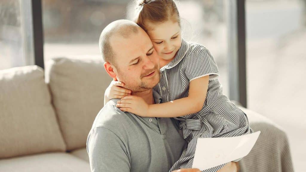 A father holding his daughter while reading a paper together.
