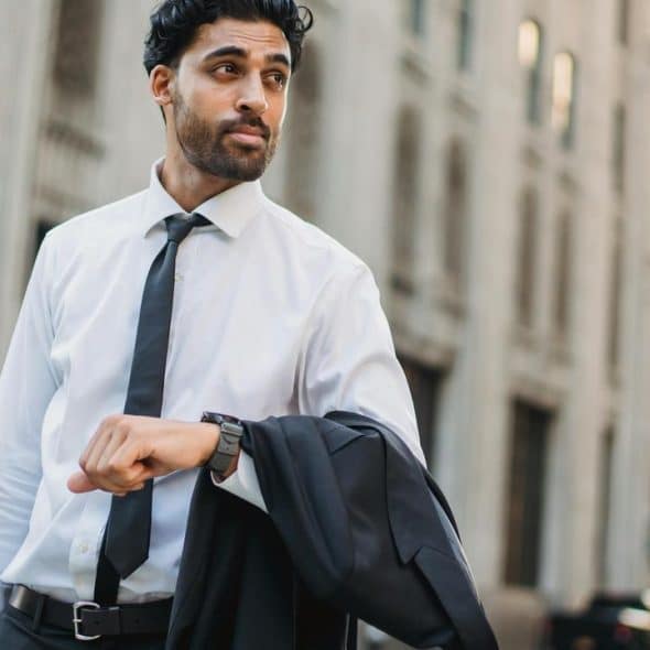 A man in a shirt and tie checking his watch.