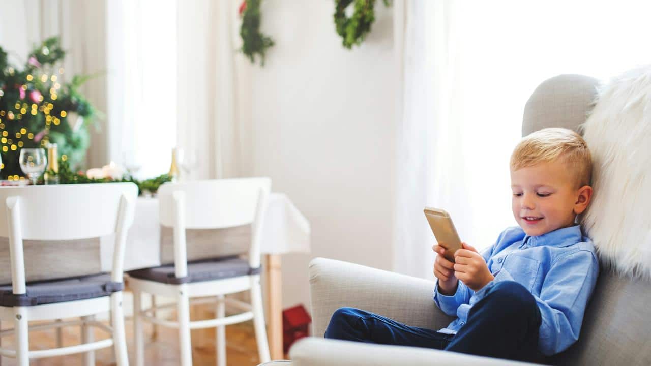 A boy smiling at a phone in a festive room.