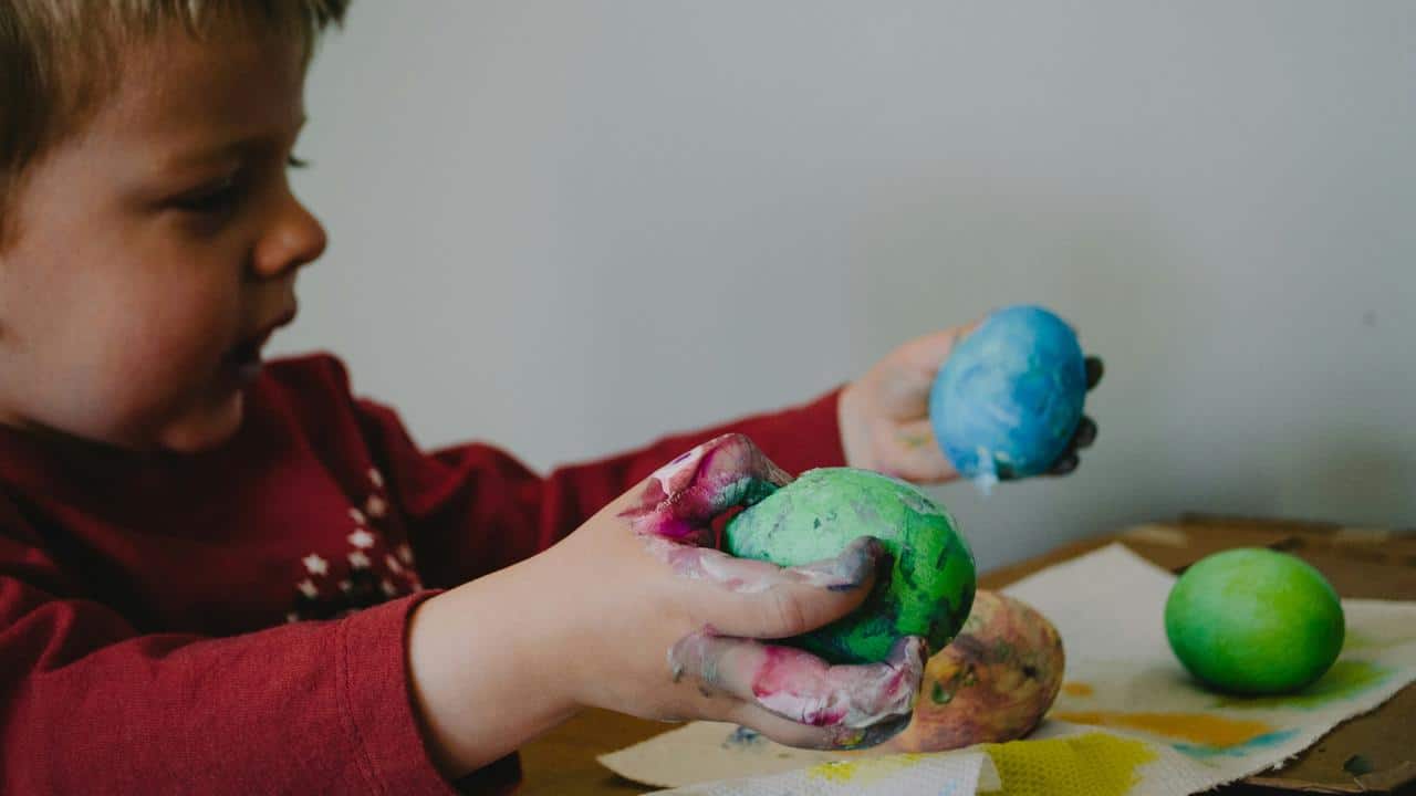 A child holding painted eggs with messy hands.