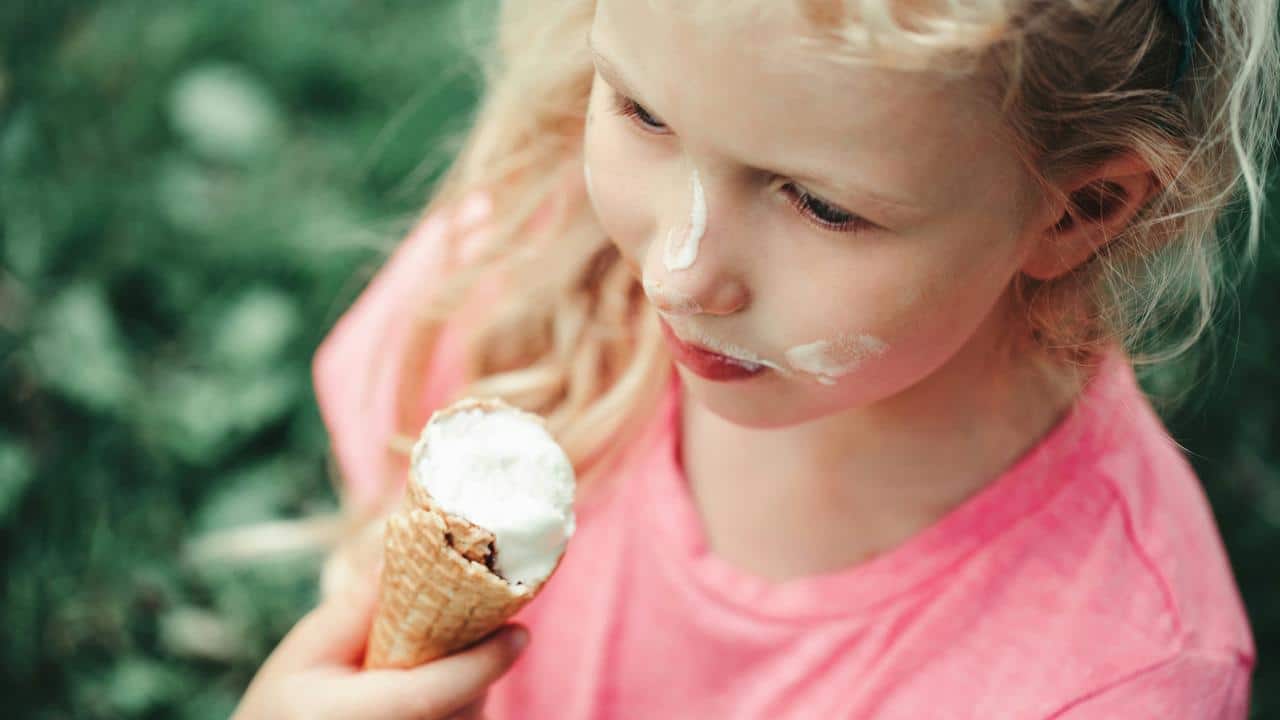 A girl with ice cream on her face holding a cone.