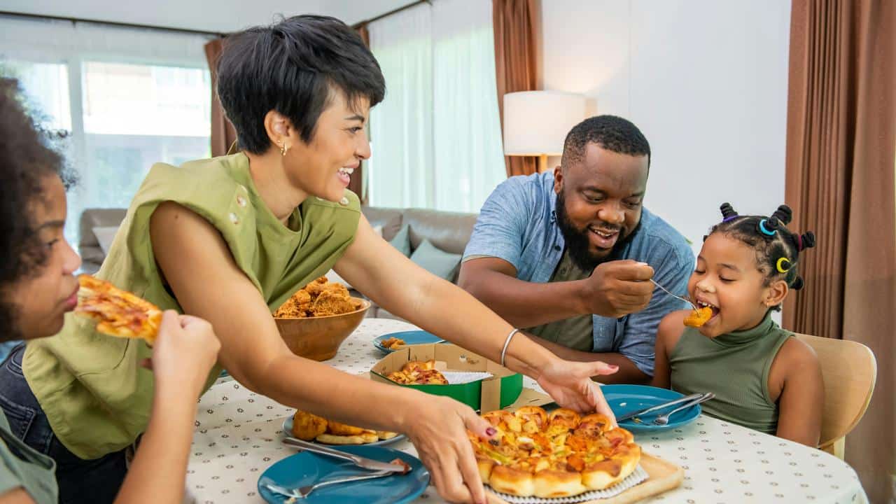 A family enjoying pizza and chicken at the dinner table.