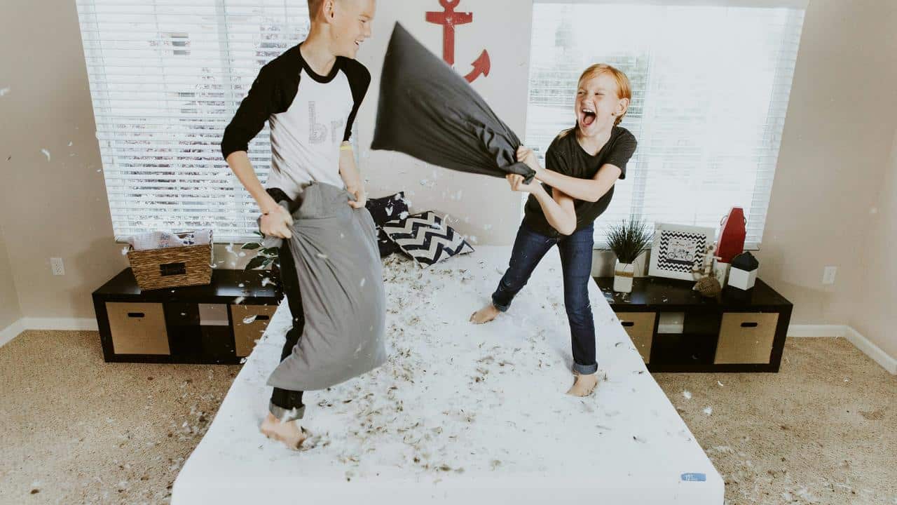 A pillow fight between two kids on a bed.