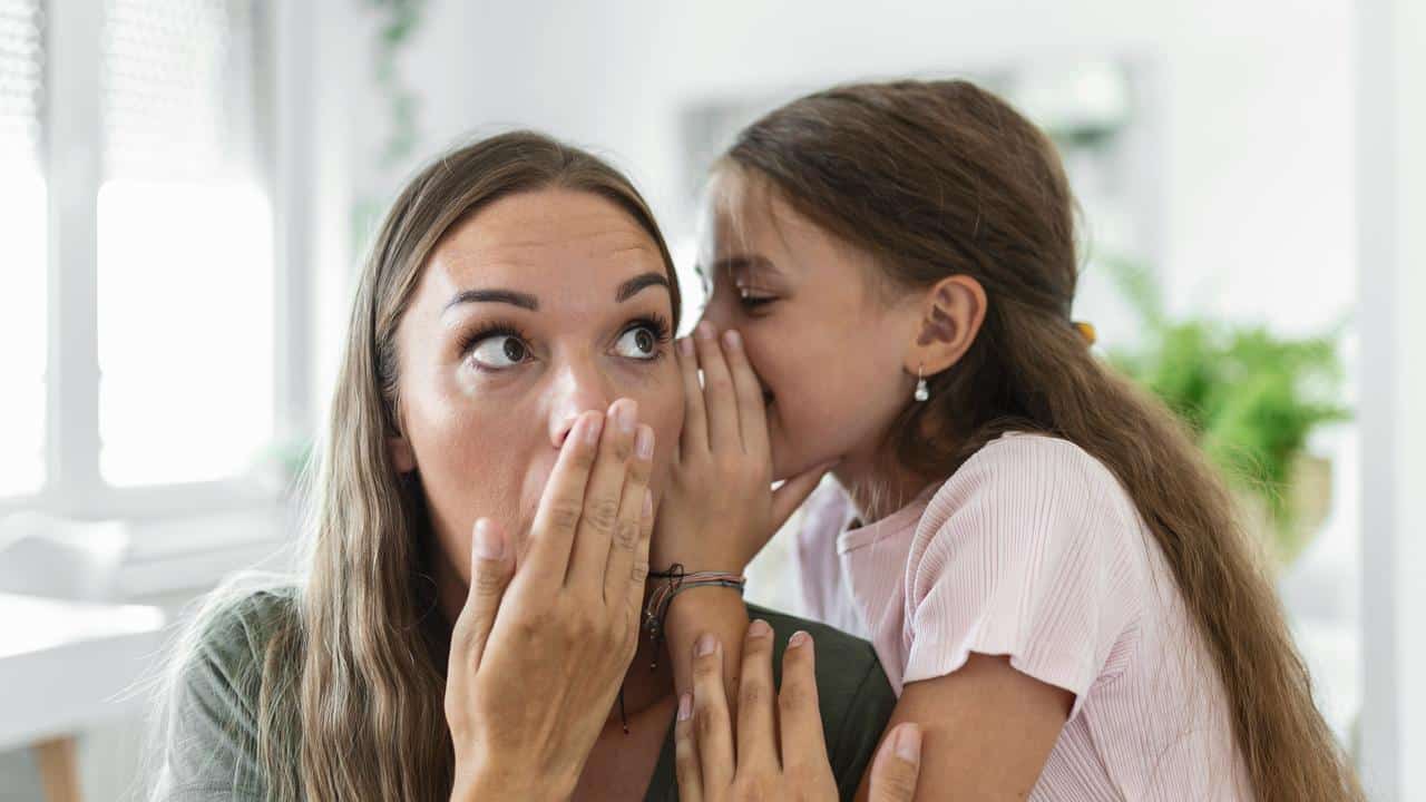 A girl whispering a secret to a surprised woman.