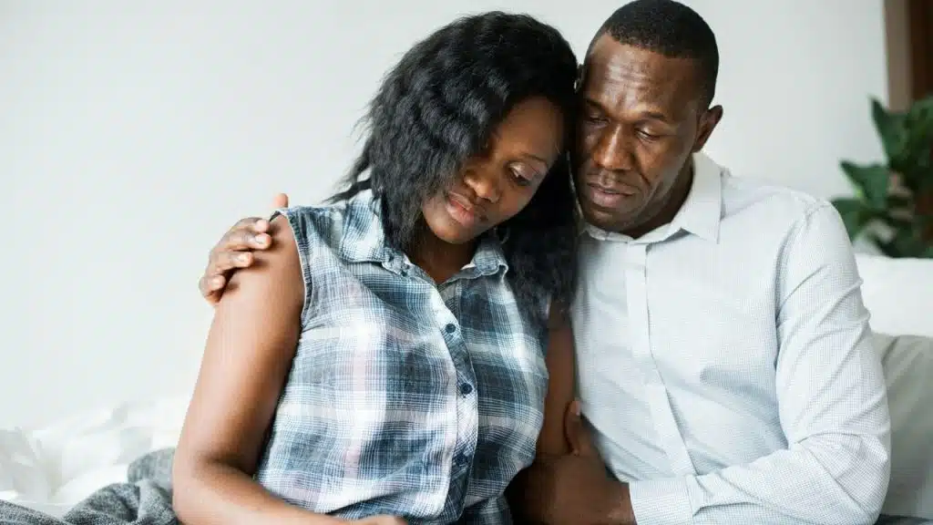 A concerned man with his arm around a sad woman's shoulders, comforting her.