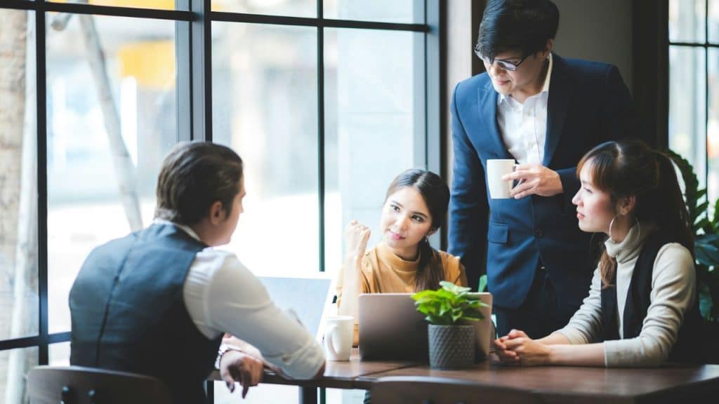 A diverse group of colleagues gather around a table discussing work-related matters.