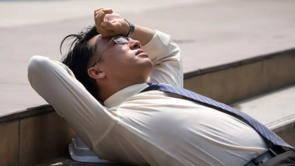 A stressed businessman lying outside with his arm over his eyes.