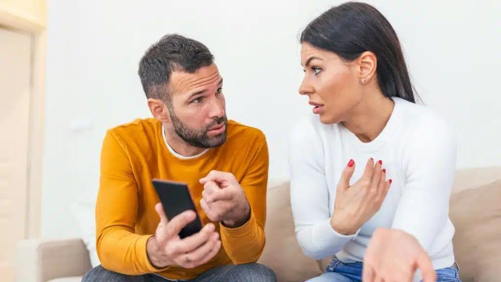 A woman gestures with her hands as a man holds his phone and speaks to her.