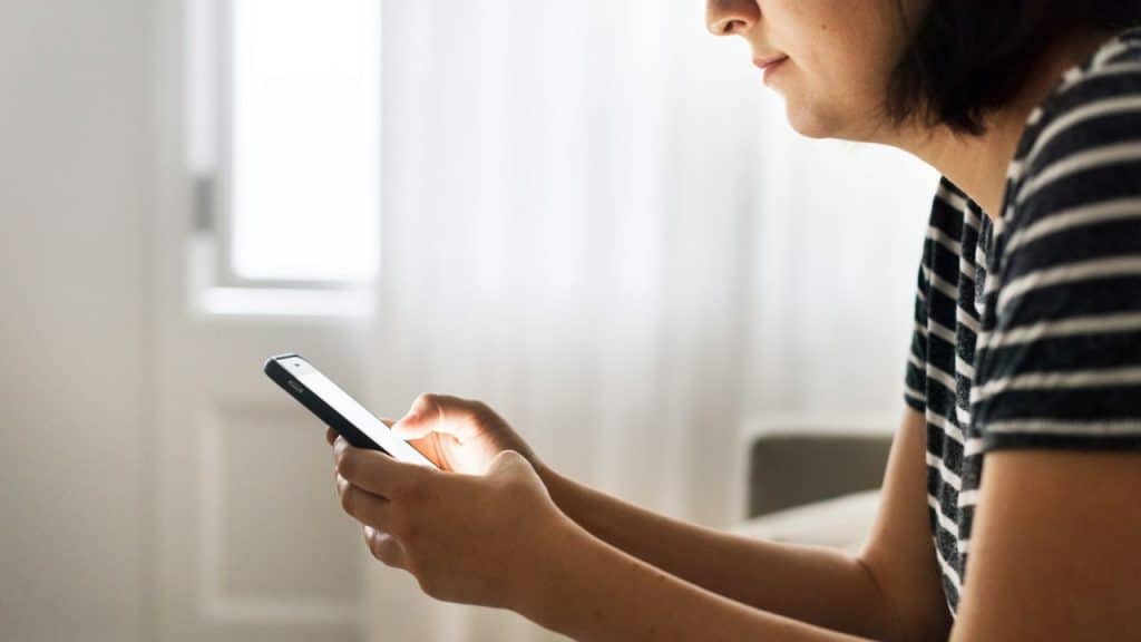 A woman holding and looking at a smartphone with a brightly lit screen.