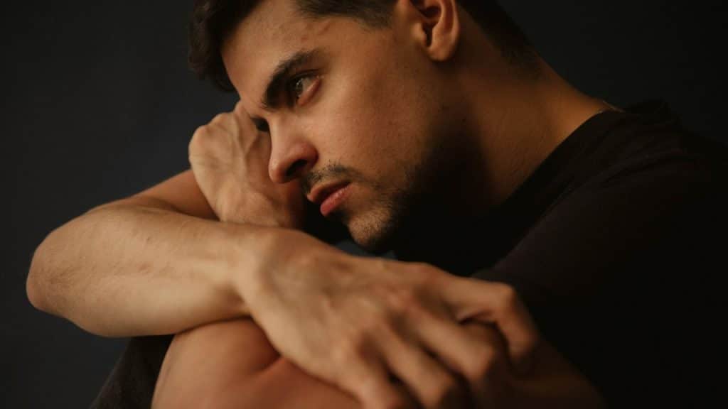 A close-up of a thoughtful, sad-looking man with his arms resting on his knees.