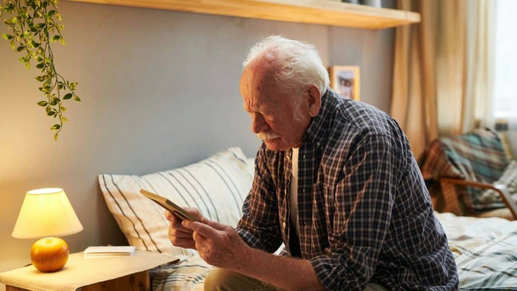 A serious elderly man with a mustache and white hair looking at a photo in a bedroom.