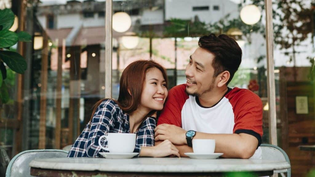 A happy couple sits at a cafe table, looking lovingly at each other.