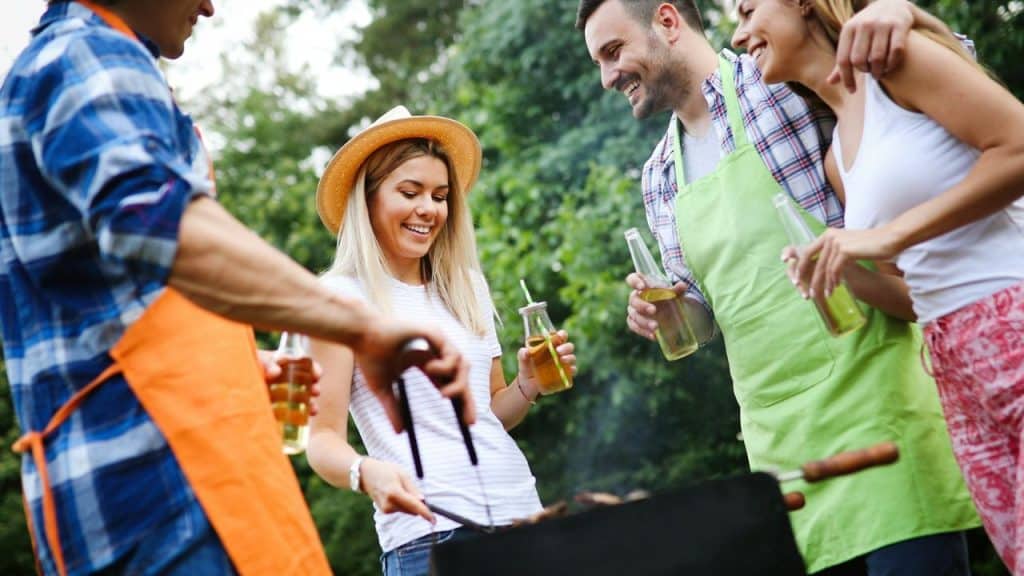 A cheerful group of friends barbecues outdoors, smiling and laughing together.