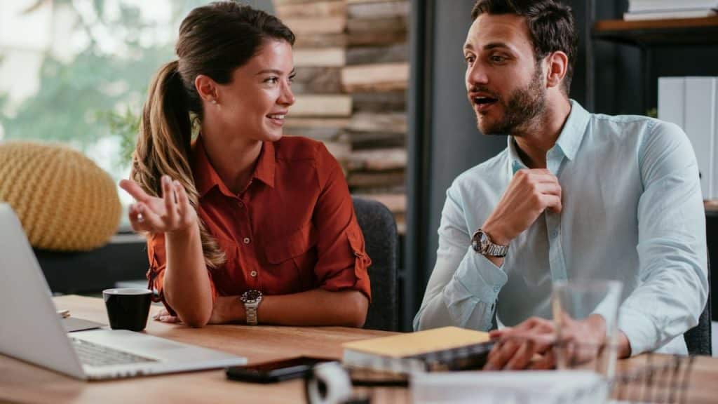 A happy couple sitting at a desk, engaged in an animated conversation.