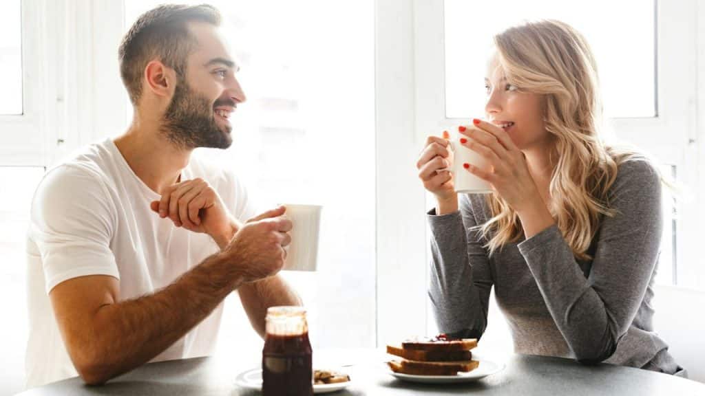 A cheerful couple smiles at each other while having breakfast and coffee.