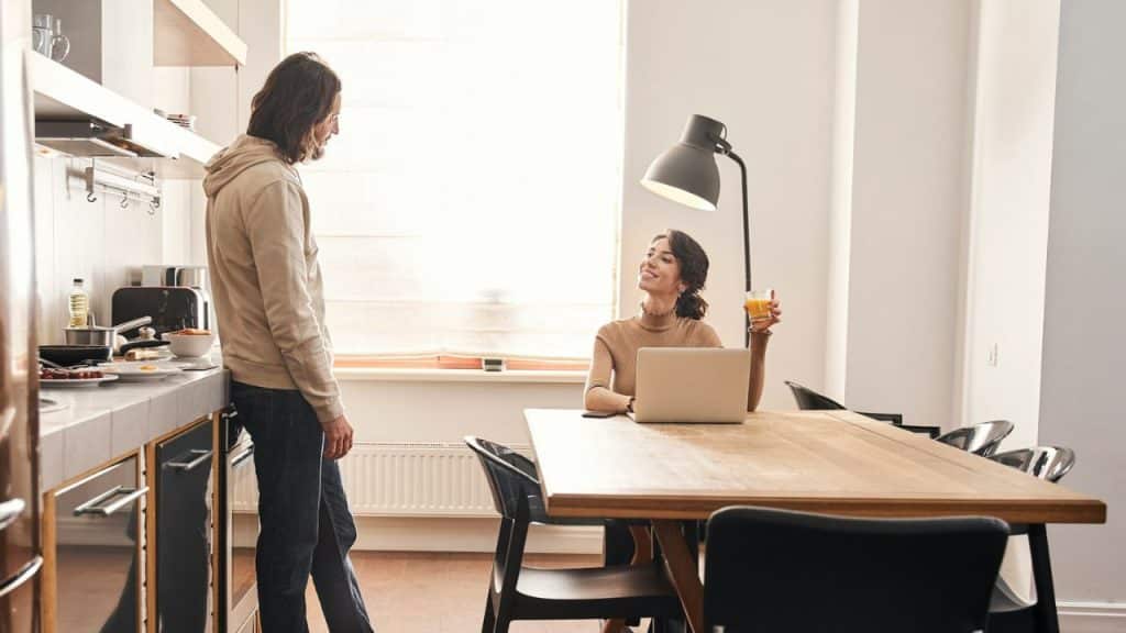 A smiling couple talks to each other while in a bright kitchen.
