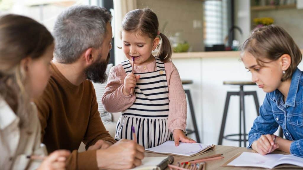 A father and his two daughters are drawing and coloring at a table.