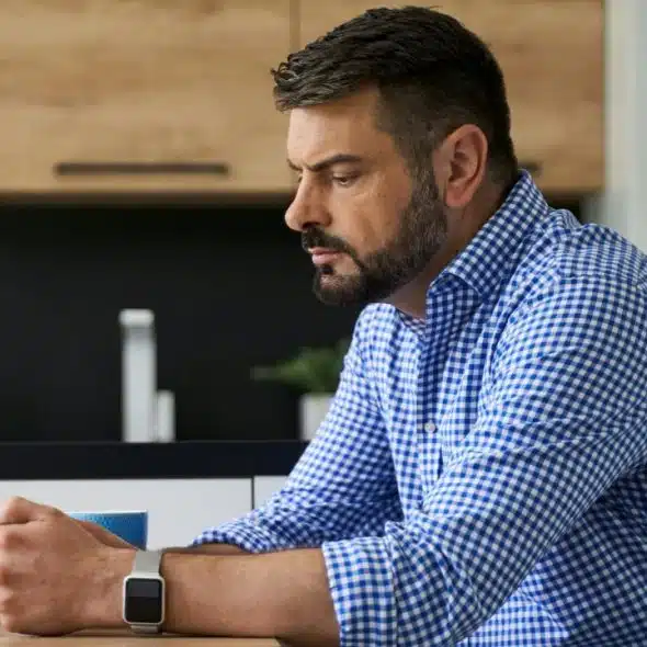 A focused man with a beard sits at a table, using his phone.
