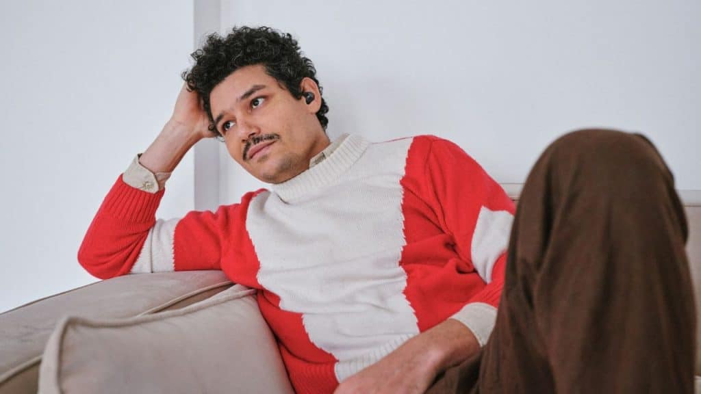 A bored man in a red and white sweater sits on a couch.