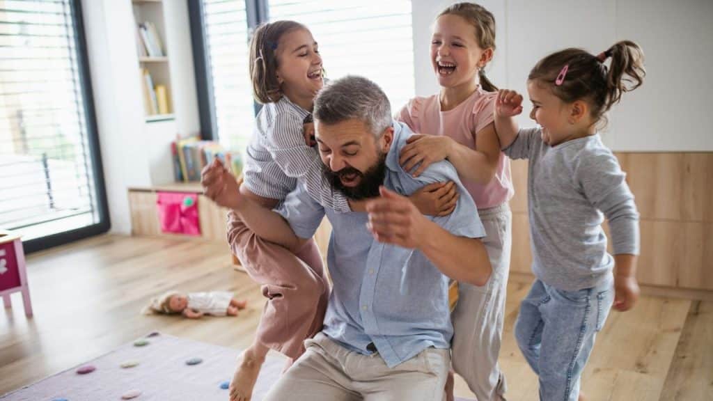 A man is being tackled and hugged by his three daughters.
