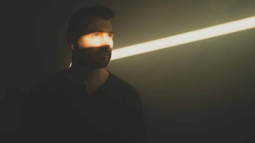 A man's face is partially lit by a diagonal beam of sunlight.