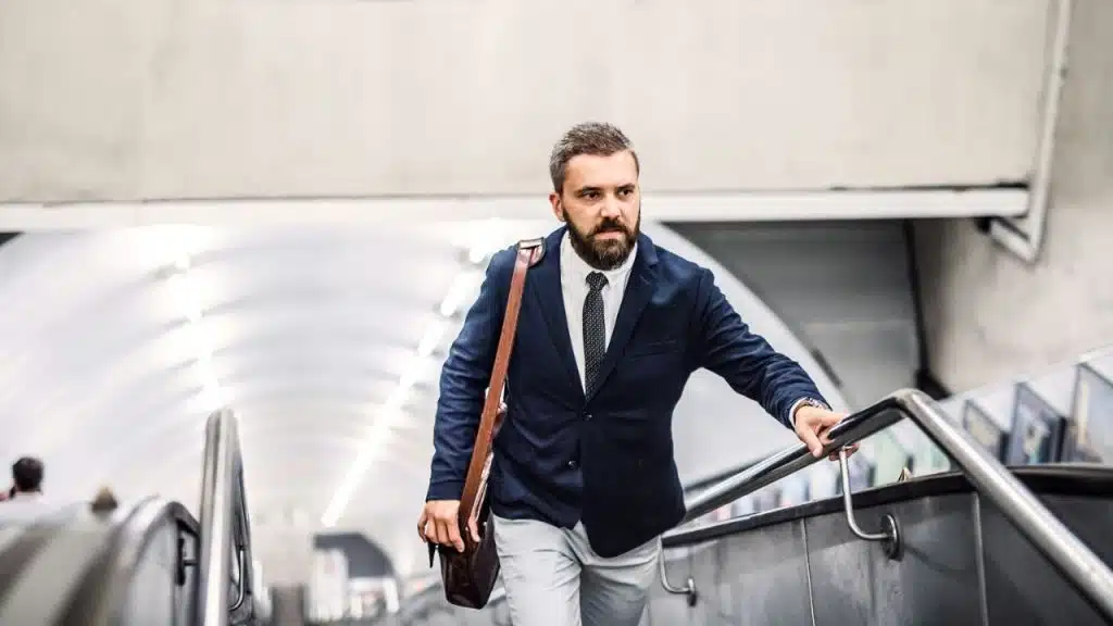 A businessman with a beard walks up an escalator, holding a briefcase.