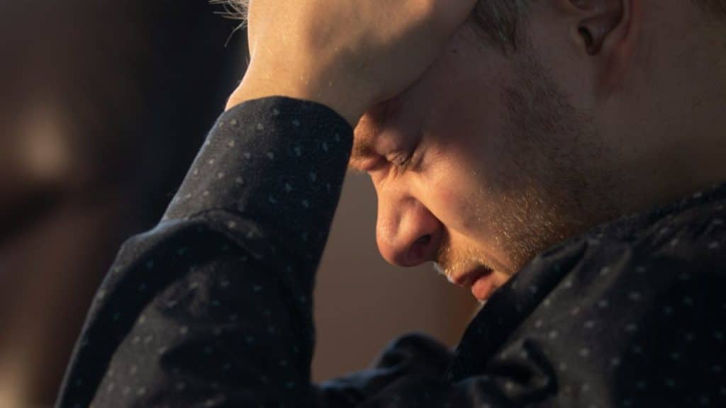 A stressed man with his eyes closed and his hand on his forehead.
