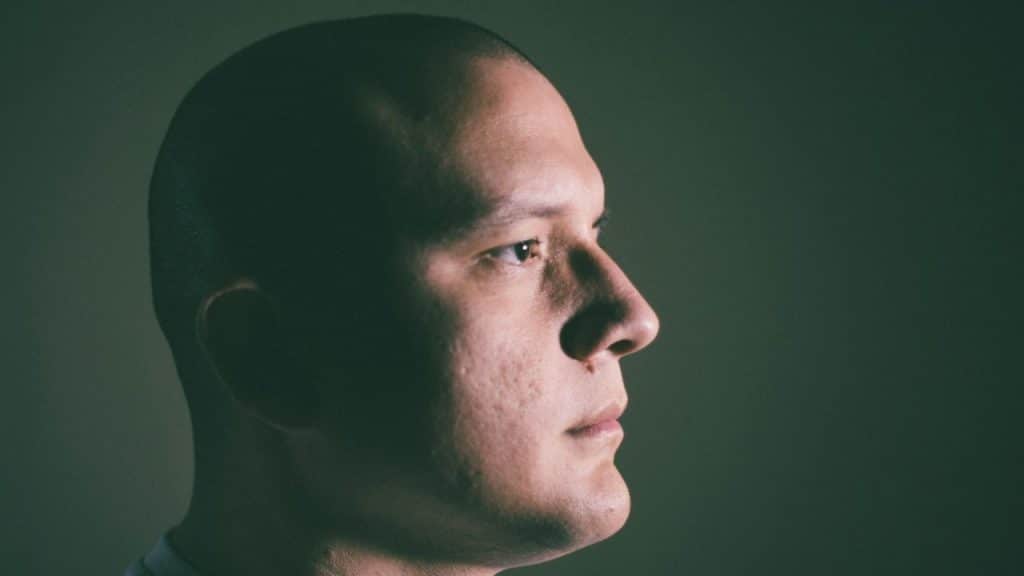 A side profile of a serious-looking man with a shaved head.