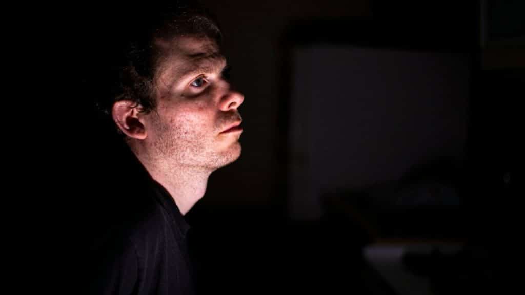 A thoughtful man's face is lit from the side in a dark room.