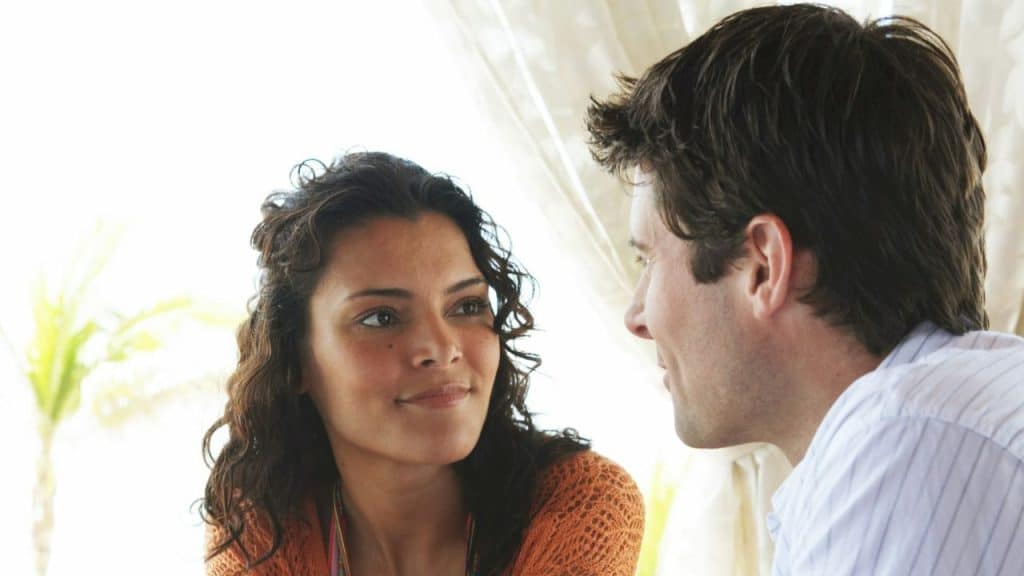 A woman with curly dark hair looks at a man with dark hair, both smiling.