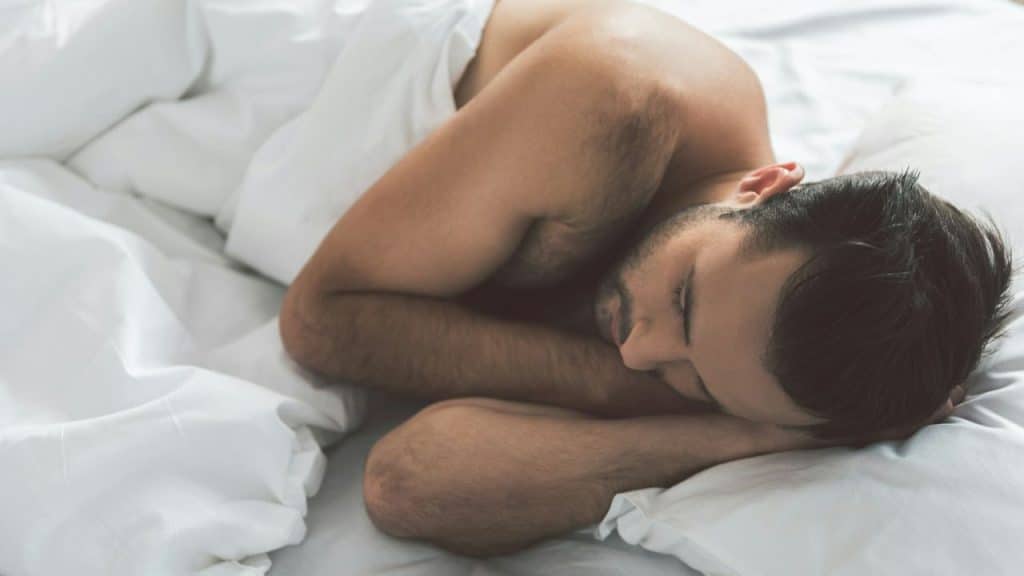 A close-up of a man sleeping peacefully on his side under a white blanket.